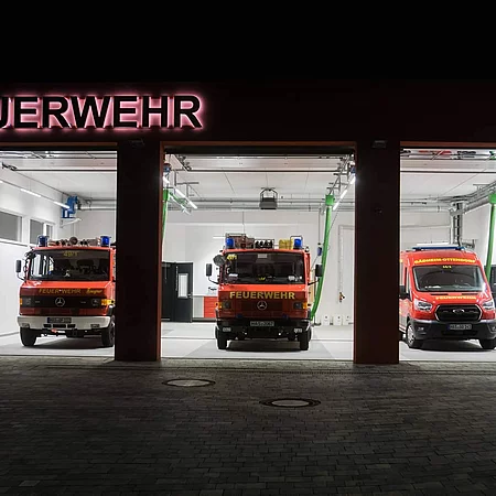 Einfahrt der Feuerwehrwache mit offenen Toren und geparkten Feuerwehreinsatzwagen.
