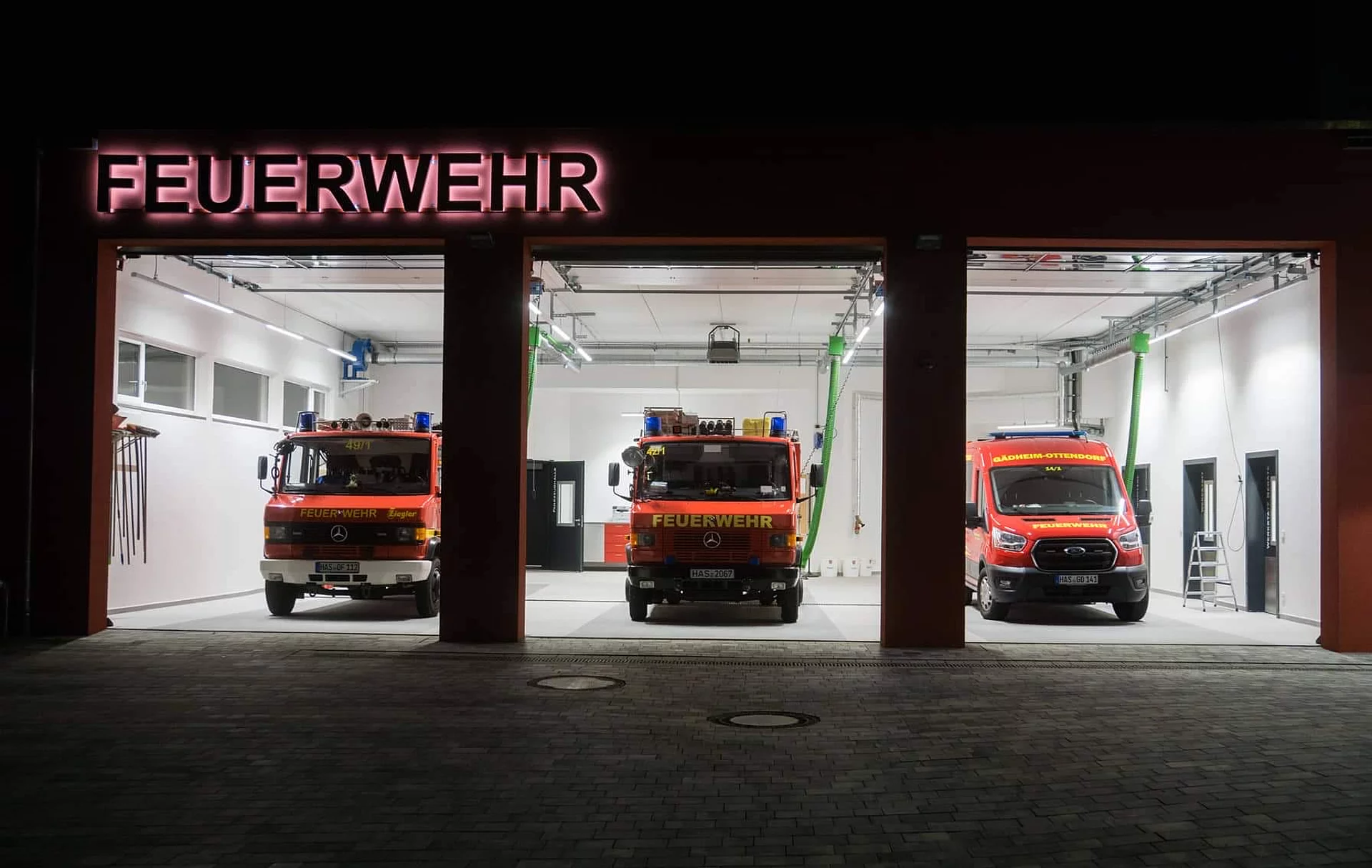 Einfahrt der Feuerwehrwache mit offenen Toren und geparkten Feuerwehreinsatzwagen.