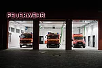 Einfahrt der Feuerwehrwache mit offenen Toren und geparkten Feuerwehreinsatzwagen.