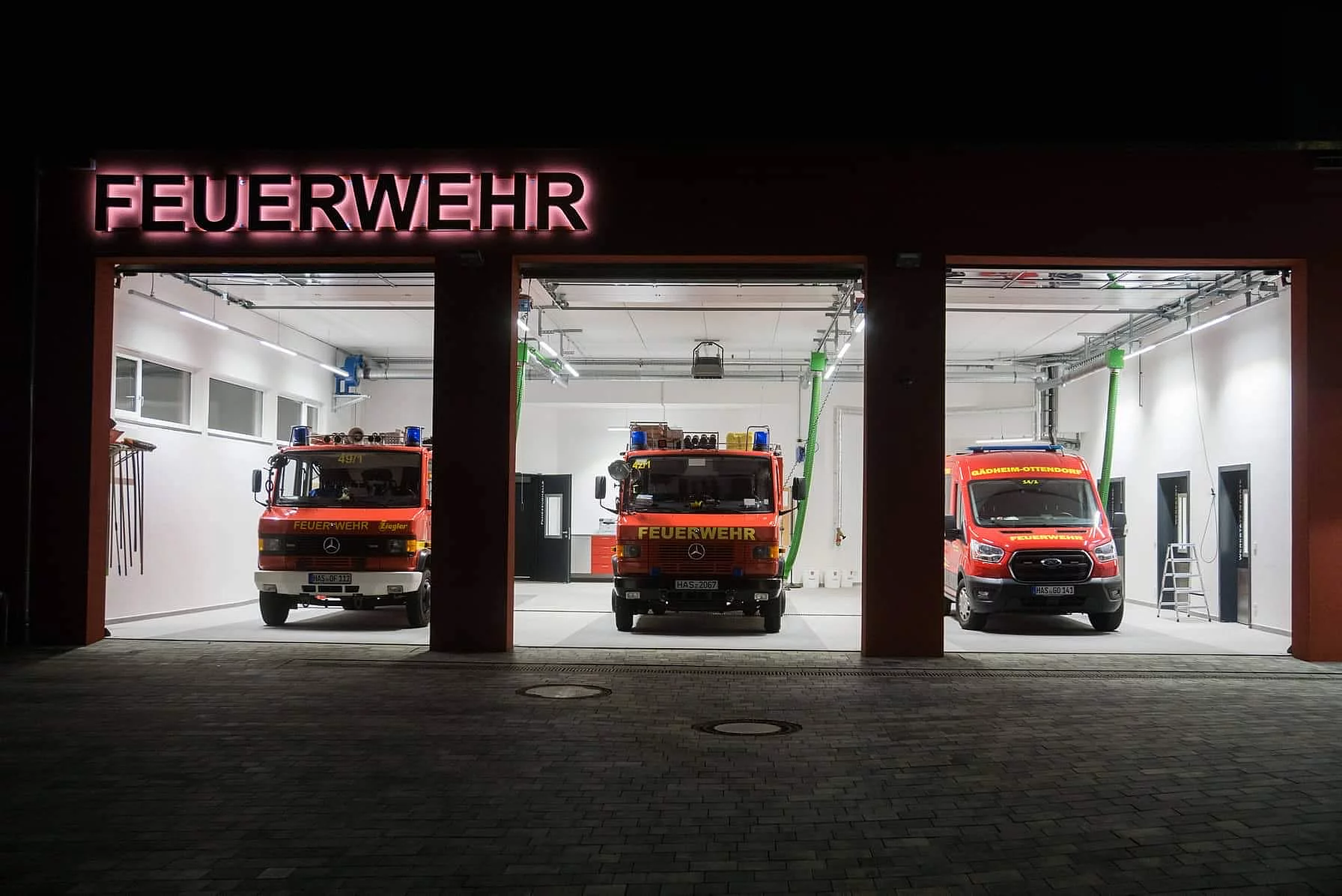 Einfahrt der Feuerwehrwache mit offenen Toren und geparkten Feuerwehreinsatzwagen.